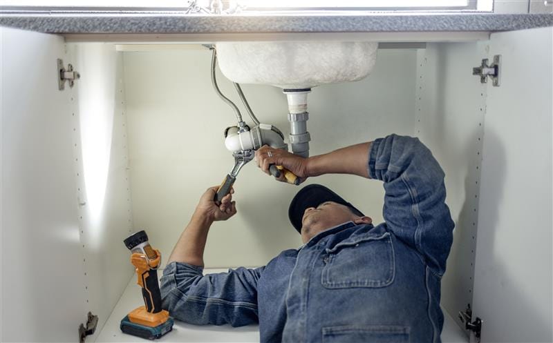 Plumber repairing pipes beneath a bathroom sink in Riverview