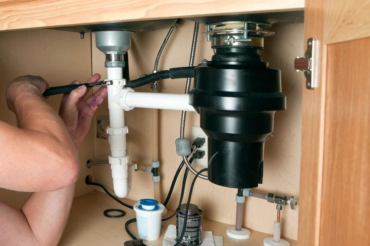 Plumber installing a garbage disposal beneath a kitchen sink in Riverview