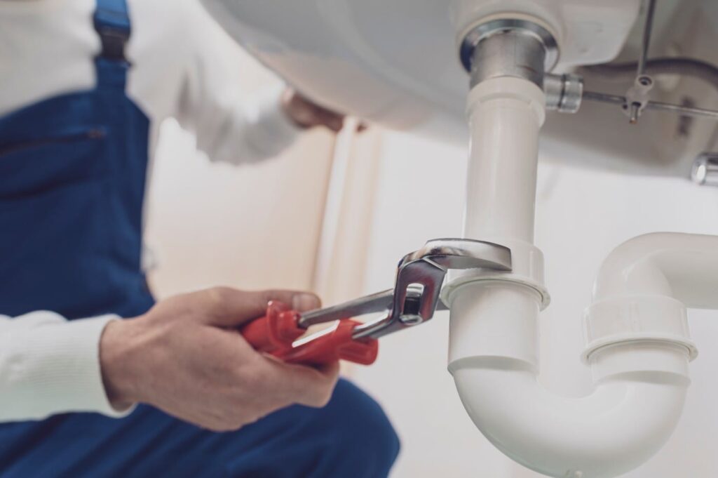 Plumber repairing a white drain pipe beneath a sink in Riverview