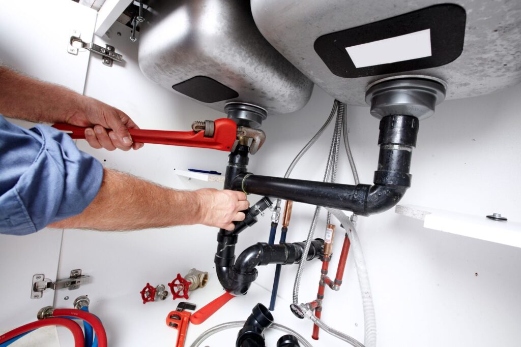 Plumber repairing drain pipes beneath a kitchen sink in Riverview